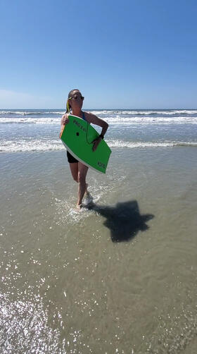 A person holding a boogie board running out of the surf.
