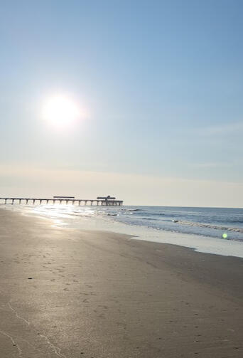Beach with Duncan Sun low over the ocean beside Folly Beach Pier on a calm morning.