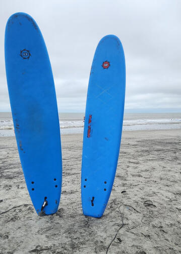 Young at heart surfer holding two bright blue foam surfboards on the beach.