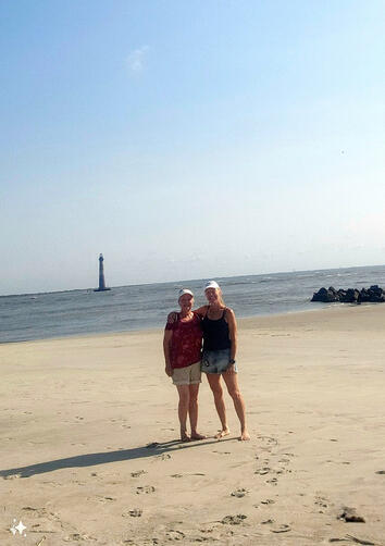 Friends posing for a picture on the beach near a distant lighthouse under a clear sky